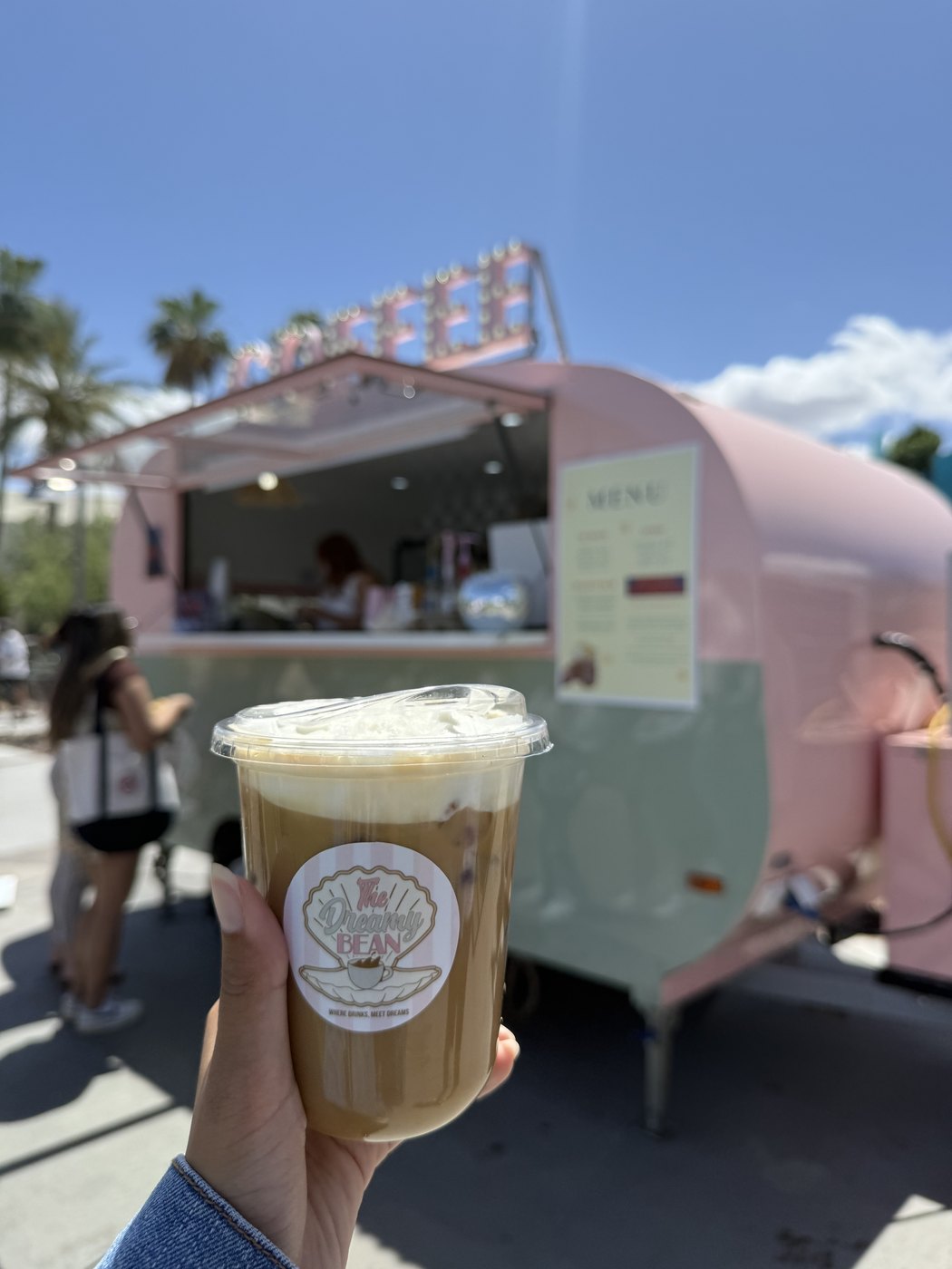 Iced coffee held in front of a pink coffee truck